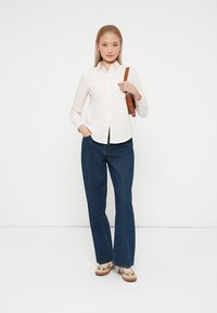 Cămășă roz deschis cu mâneci lungi, asociată cu blugi evazați de culoare albastru închis. Include o geantă maro cu umăr.