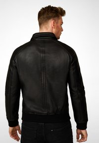 Black leather jacket with a high collar, ribbed cuffs, and a smooth texture. Features clean lines and a tailored fit.
