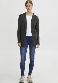 Mörkgrå cardigan i strukturerad stickad kvalitet, med öppen frontdesign, matchad med en vit T-shirt, blå tajta jeans och ljusa sneakers.