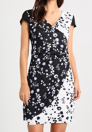Femme portant une robe fleurie longueur genou avec des panneaux contrastés noirs et blancs et des manches courtes noires style casquette.