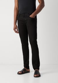 Czarne jeansy z denimu o dopasowanym kroju, pięcioma kieszeniami i zapinane na guziki, zestawione z czarnymi sandałami z teksturowanym paskiem.