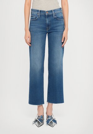 Wide-leg blue denim jeans with a raw hem, featuring a mid-rise waist and classic five-pocket design. Paired with metallic shoes.