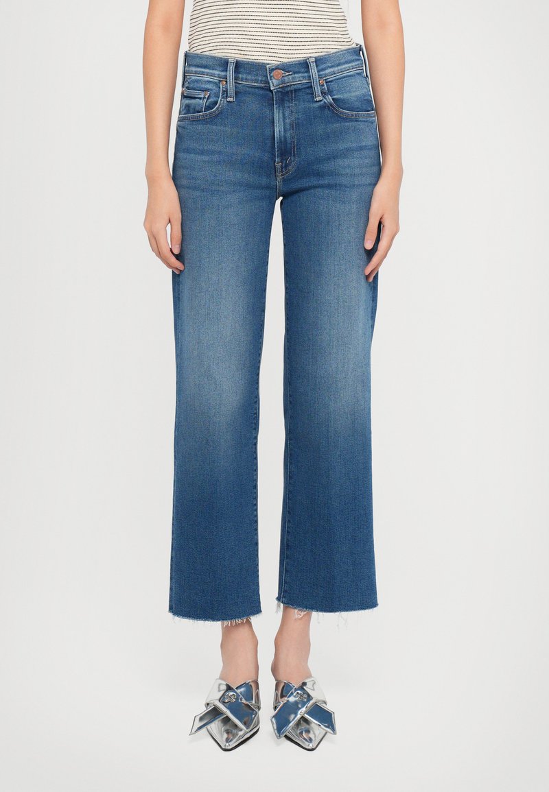 Jeans in denim blu a gamba larga con orlo grezzo, caratterizzati da una vita a media altezza e design classico a cinque tasche. Abbinati a scarpe metalliche.