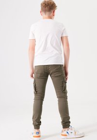Grüne Cargo-Hosen mit gerippten Bündchen, Seitentaschen und schmaler Passform, kombiniert mit einem schlichten weißen T-Shirt und weißen Sneakern mit orangefarbenen Akzenten.