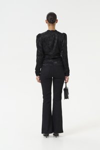Black textured blouse with puff sleeves, paired with black flared jeans. The model holds a small black handbag and wears high-heeled shoes.