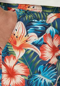 Kleurrijke zwembroek met een bloemenpatroon van rode, oranje en blauwe hibiscusbloemen op een donkerblauwe achtergrond. Gladde textuur.