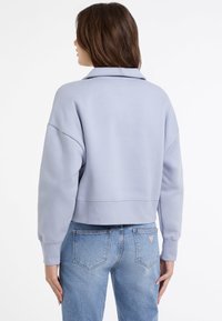 Felpa cropped azzurra con colletto, maniche oversize e una texture morbida, abbinata a jeans azzurri.