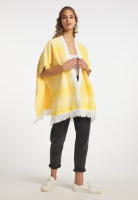 Żółty kimono w wzór z chevronem, z białym frędzelkowym dołem i otwartym przodem. W połączeniu z ciemnymi spodniami i białymi sneakersami.
