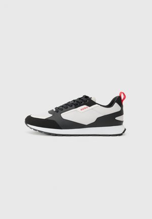 Black and white sneakers with a suede and mesh upper, featuring a red pull tab and textured sole. Lace-up design with logo detail.