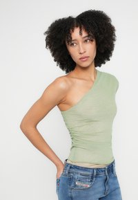 Ühe õlaga, heleroheline top küljetikkudega, valmistatud siledast kangast, kombineeritud siniste teksapükstega.