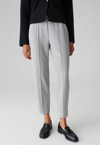 Pantalon gris clair sur mesure avec une taille à cordon de serrage, comportant des plis à l'avant et un design court, associé à des mocassins noirs.