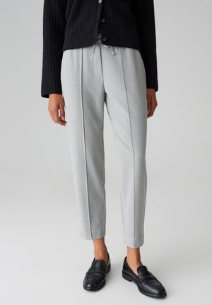 Pantaloni grigi chiari su misura con vita regolabile, caratterizzati da pences frontali e un design cropped, abbinati a mocassini neri.