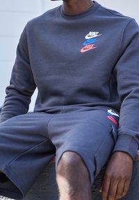 Mörkblå sweatshirt med rundad halsringning och färggrafik av Nike-logotypen. Matchas med shorts i samma färg som har sidofickor och logodetalj.