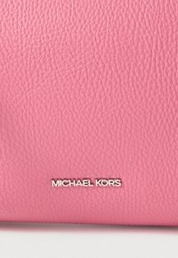 Różowy portfel z teksturowanej skóry z srebrnym logo "MICHAEL KORS" na dole. Materiał ma ziarnistą fakturę.