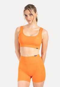 Oranje sportcrop top en hooggetailleerde shorts gemaakt van glad, rekbaar materiaal. Voorzien van een subtiel logo en een naadloos ontwerp.
