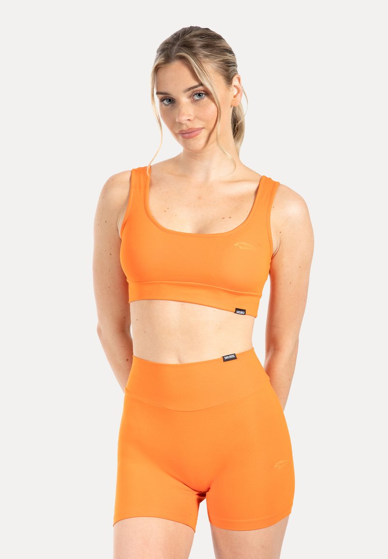 Oranje sportcrop top en hooggetailleerde shorts gemaakt van glad, rekbaar materiaal. Voorzien van een subtiel logo en een naadloos ontwerp.