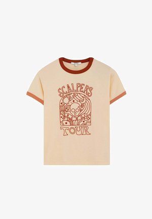 Camiseta beige de manga corta con ribetes color óxido, que presenta un gráfico de calavera y líneas onduladas, junto con el texto "Scalpers Tour" en el mismo color óxido.