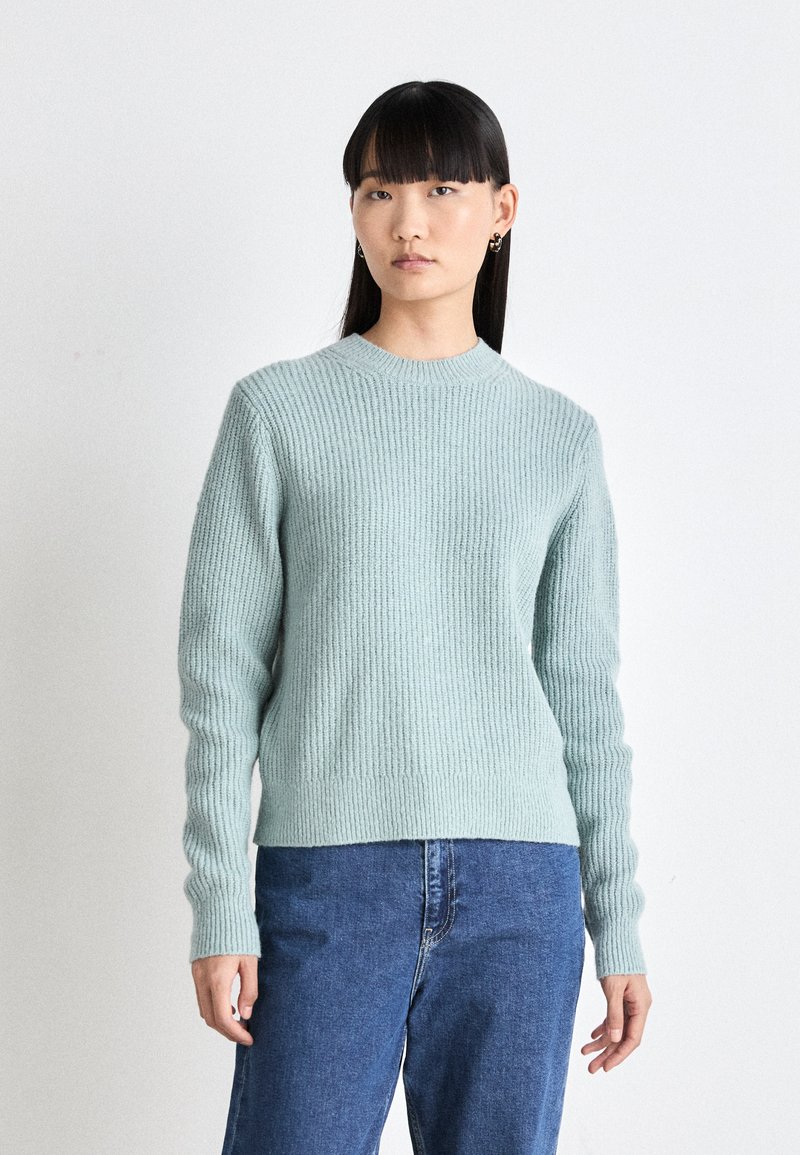 Hellblauer gerippter Strickpullover mit langen Ärmeln und rundem Ausschnitt, kombiniert mit hochtaillierten blauen Jeans.