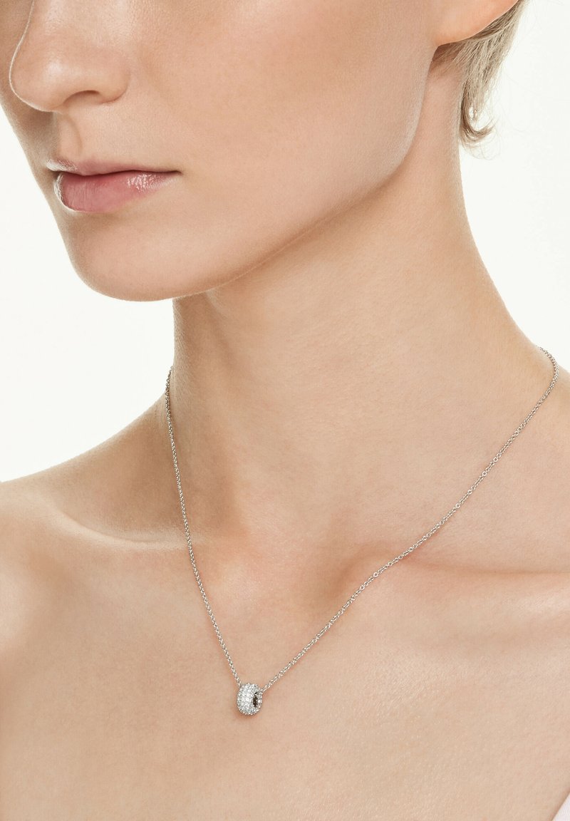 Sølv halskæde med en rund vedhæng, der har en klynge af små, glitrende sten, som hviler på en glat hals.