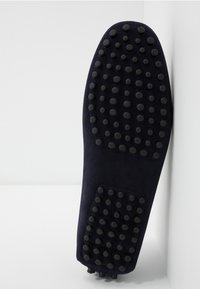 Navy ruskindsko sålen har hævede cirkulære grebsmønstre, der giver godt fodfæste. Designet er fladt med en kontureret profil for komfort.