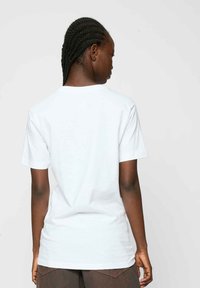 T-shirt en coton blanc à manches courtes, avec un col rond et une coupe décontractée, présentant une texture lisse et uniforme. Pas de logos ni de motifs visibles.