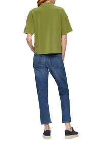 Olivgrünes, kurzes T-Shirt mit kurzen Ärmeln, kombiniert mit blauen Jeans. Die Jeans haben einen geraden Schnitt und Gesäßtaschen. Schwarze Sneakers vervollständigen den Look.