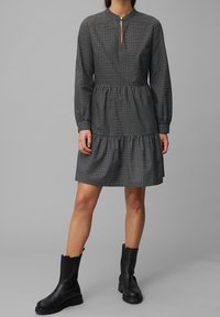 Zwart-wit geruite jurk met een hoge halslijn, lange mouwen en een roklagen, gecombineerd met zwarte enkellaarsjes.