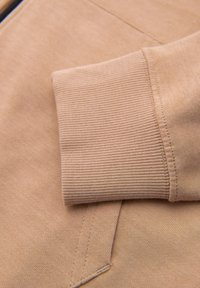 Manche beige à manches longues avec poignet côtelé reposant sur un tissu assorti avec coutures visibles et détails de couture.