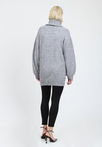 Grå oversized sweater med cowl neck, blød tekstur, ribstrikkede manchetter og kant; parret med sorte leggings og mønstrede højhælede sko.