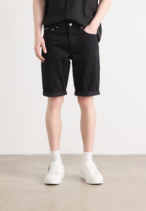 Shorts en denim noir avec bords roulés, design à cinq poches et quincaillerie argentée. Assortis à des baskets blanches et des chaussettes de longueur mi-mollet.