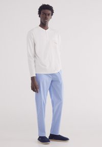 Camicia bianca a maniche lunghe con taschino sul petto, abbinata a pantaloni a righe blu chiaro e scarpe slip-on blu navy. Semplicità nel design e nei colori.