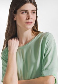Lysegrøn kortærmet top med rund halsudskæring. Glat stof, afslappet pasform og diskrete syningsdetaljer på ærmerne.