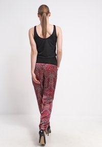 Svart ärmlös topp matchad med livfulla röda byxor med paisleymönster. Byxorna har en lös passform och är kombinerade med svarta högklackade skor.