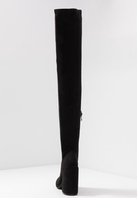 Bottes noires au-dessus du genou en daim doux, avec un talon haut épais, un bout pointu, et une fermeture éclair latérale pour un enfilage facile.