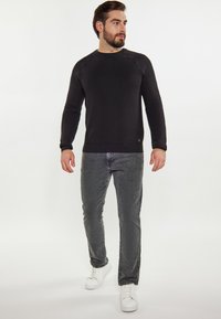 Zwarte lange mouw sweatshirt met een ronde hals, gecombineerd met grijze tapered jeans en witte sneakers. Glad textuur, minimalistisch ontwerp, geen patronen.