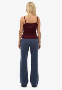 Bordowy top bez rękawów z cienkimi ramiączkami, zestawiony z luźnymi, granatowymi spodniami typu wide-leg z wysokim stanem. Gładka tekstura i luźny krój.