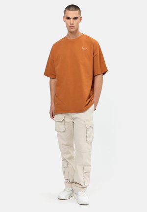 Hnědé oversized tričko s malým logem, spárované s béžovými cargo kalhotami s vícero kapsami a bílými teniskami.