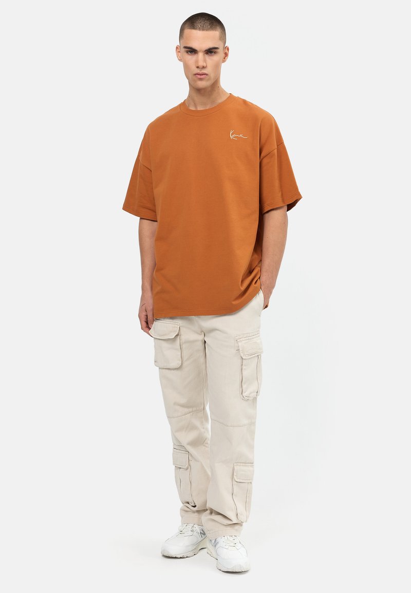 Hnedé oversized tričko s malým logom, skombinované s béžovými cargo nohavicami s viacerými vreckami a bielymi teniskami.
