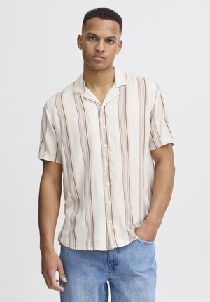 Korte ermerskjorte i kremhvit med vertikale brune striper. Knapp-ned design, lett stoff og avslappet passform. Brukt med blå denimshorts.