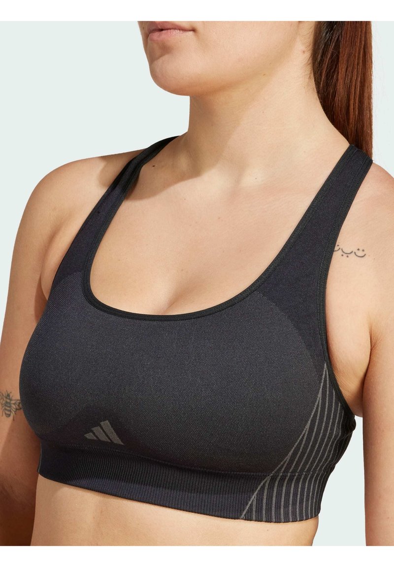 Soutien-gorge de sport noir avec une finition lisse et texturée. Doté de bretelles larges, d'un décolleté arrondi et d'un motif rayé subtil sur le côté.