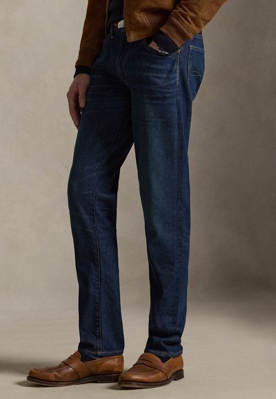 Dunkelblaue Jeans aus Denim mit geradem Schnitt, dezentem Farbverlauf und klassischem Fünf-Taschen-Design, kombiniert mit braunen Leder-Slippern.