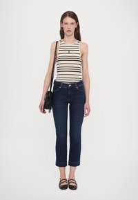 Gestreept tanktop in beige en zwart, gecombineerd met donkerblauwe cropped jeans. Model houdt een kleine zwarte handtas vast en draagt zwarte flats.
