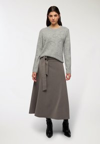 Szary sweter z dekoracyjnymi, ćwiekowanymi kokardami, w połączeniu z brązową, wysoką spódnicą w stylu kopertowym z wiązaniem oraz czarnymi, zakrytymi botkami na obcasie.