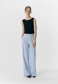 Top nero senza maniche, pantaloni a palazzo a righe blu e bianche, tessuto morbido, vita alta, tasche frontali, aderenti ai fianchi, larghi alle gambe.