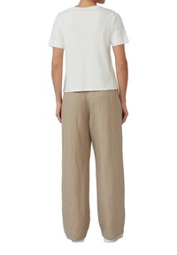 Un haut blanc à manches courtes associé à un pantalon en lin beige ample. Le haut a un design simple avec un décolleté arrondi ; le pantalon présente une finition texturée.