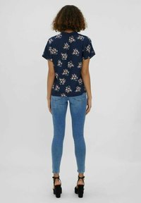 Chemise à manches courtes à fleurs bleu marine avec des fleurs de couleur claire, associée à un jean ajusté bleu clair et des sandales noires à talons.