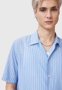 Camicia azzurra chiaro a maniche corte con righe verticali bianche, chiusura frontale con bottoni e una consistenza morbida. Collo distintivo e vestibilità casual.