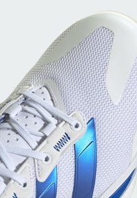 Białe sneakersy z siateczkową cholewką, niebieskimi akcentami i teksturowaną podeszwą. Posiadają płaskie sznurowadła i syntetyczne wstawki. Detale logo w kolorze srebrnym i niebieskim.