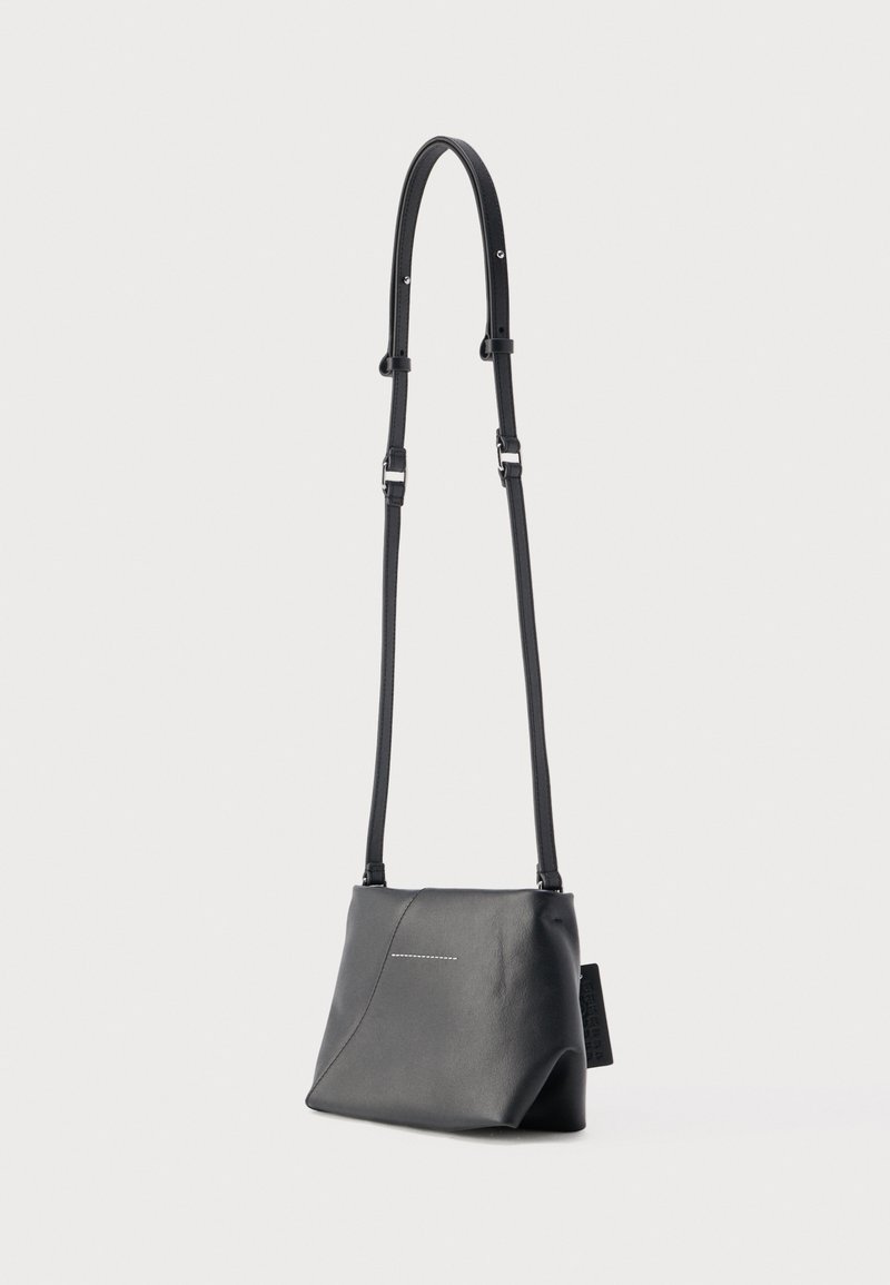 Black leather crossbody bag with adjustable strap and subtle stitched detail on front, standing against plain light background.