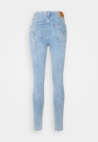 Vaaleansiniset farkkuhousut, kapeat ja istuvat, joissa on kaksi takataskua, kaartuvat saumat ja ruskea nahkainen merkkilaatta vyötäröllä.